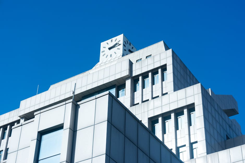 Sleek modern building with a clock tower against a vibrant blue sky, highlighting minimalistic design.